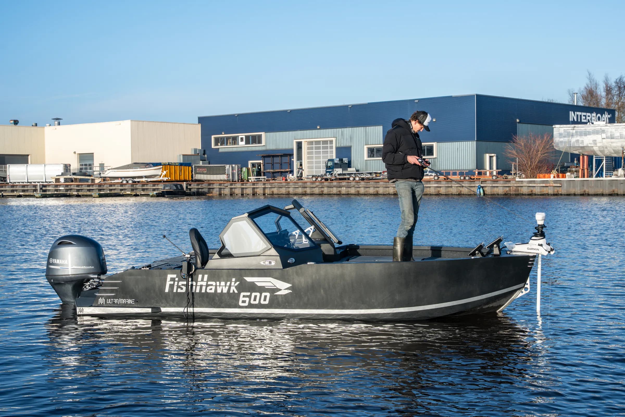 Visser staand op de FishHawk 600, hengel uitgeworpen bij een jachthaven